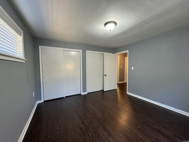 unfurnished bedroom featuring dark wood finished floors, a textured ceiling, two closets, and baseboards