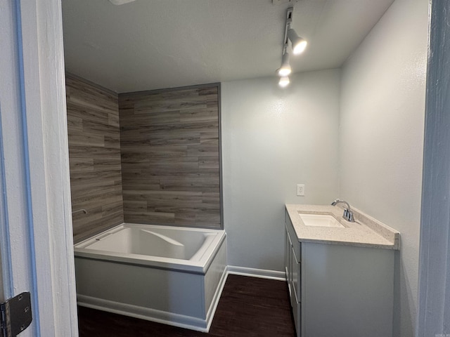 bathroom with baseboards, a tub to relax in, rail lighting, wood finished floors, and vanity