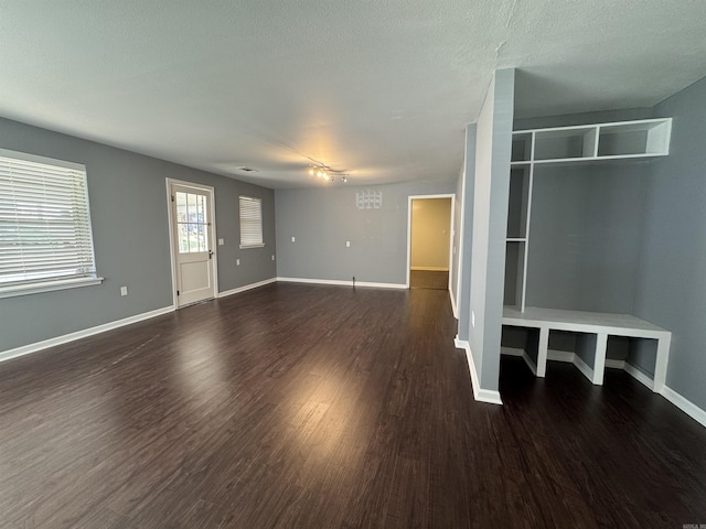 unfurnished living room with baseboards, dark wood-type flooring, and a textured ceiling