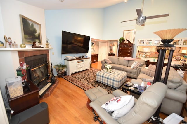 living area featuring ceiling fan, high vaulted ceiling, light wood-style flooring, and a tile fireplace