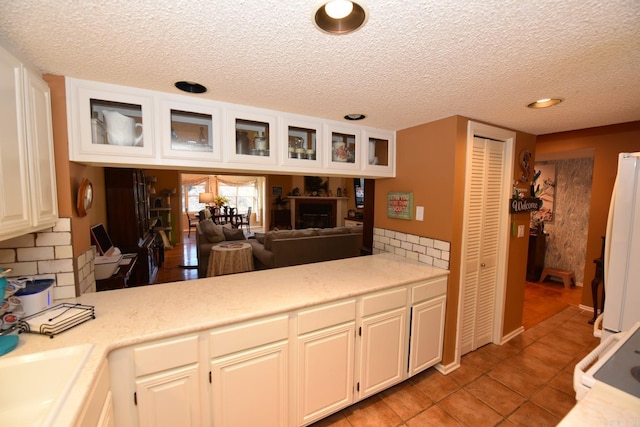 kitchen featuring light tile patterned floors, freestanding refrigerator, light countertops, glass insert cabinets, and white cabinetry