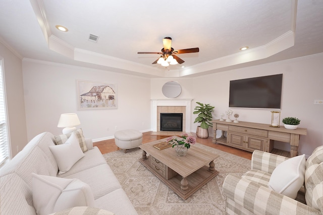 living room featuring visible vents, crown molding, baseboards, a fireplace, and a raised ceiling