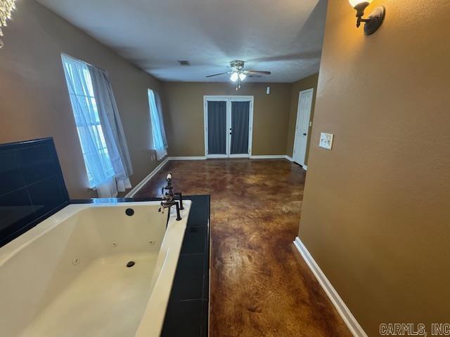 interior space featuring baseboards, a tub with jets, and a ceiling fan