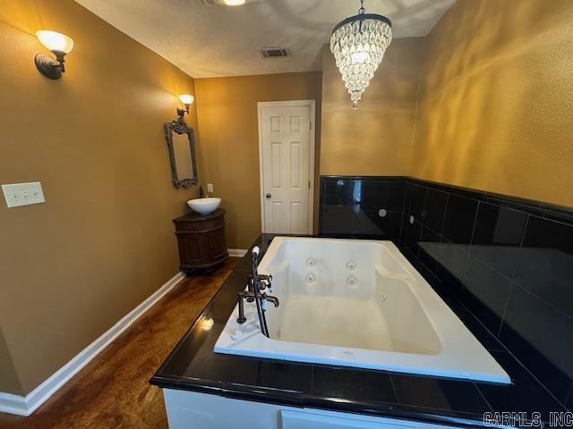 bathroom featuring a notable chandelier, visible vents, baseboards, and a tub with jets