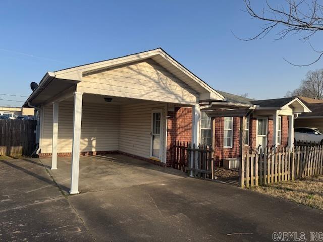 view of front of property featuring an attached carport, concrete driveway, fence, and brick siding