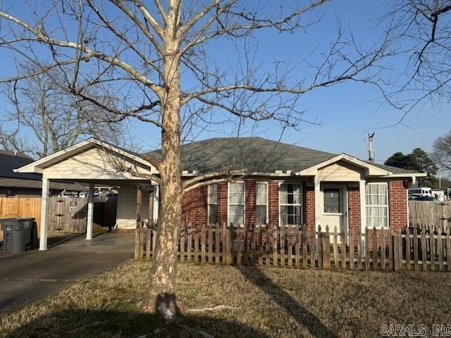 view of front facade featuring a fenced front yard, driveway, brick siding, and a carport