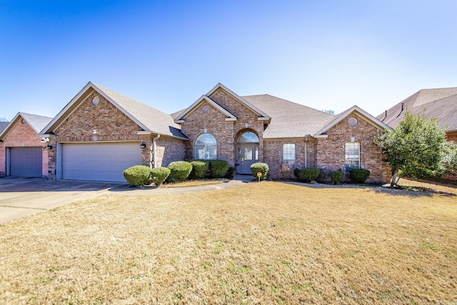 view of front of property with a front yard, driveway, roof with shingles, an attached garage, and brick siding