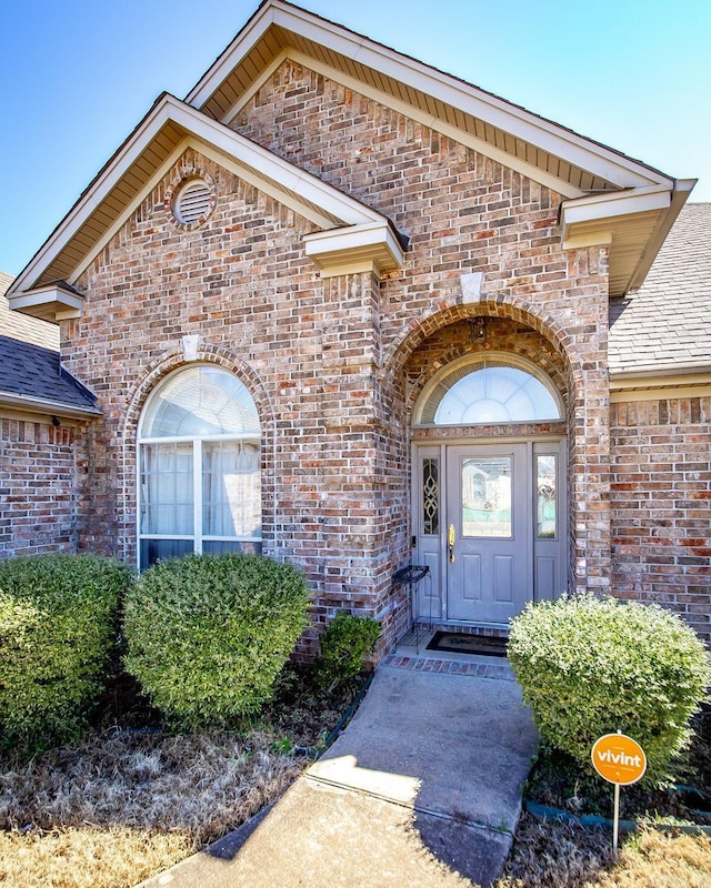 property entrance featuring brick siding and roof with shingles