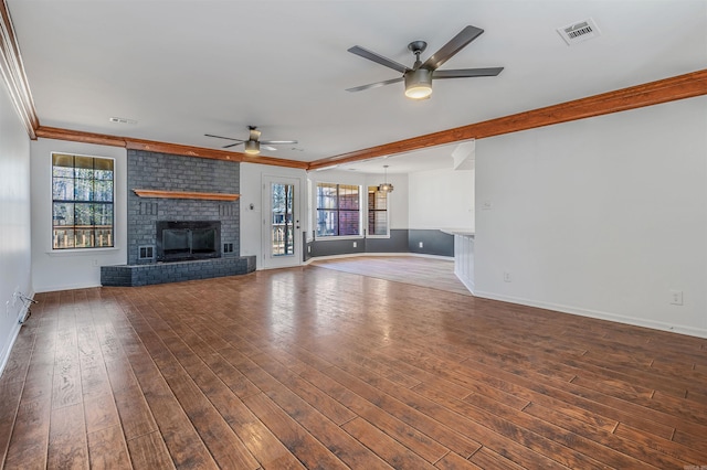 unfurnished living room with visible vents, ornamental molding, a ceiling fan, wood-type flooring, and a brick fireplace