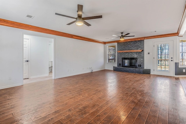 unfurnished living room with hardwood / wood-style floors, baseboards, ceiling fan, crown molding, and a brick fireplace