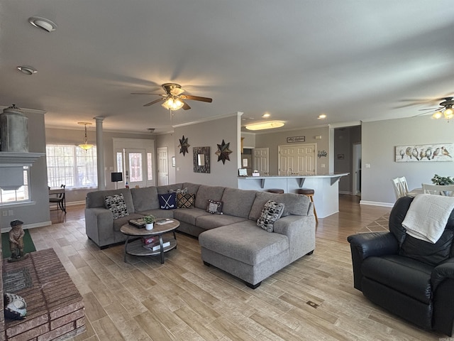 living room featuring ceiling fan, baseboards, ornamental molding, a fireplace, and light wood-style floors