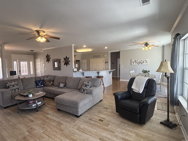 living room featuring baseboards, visible vents, light wood-style flooring, ceiling fan, and ornamental molding