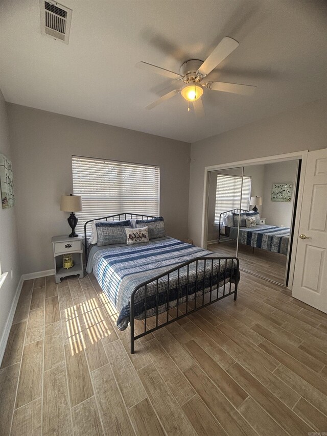 bedroom with a ceiling fan, wood finished floors, visible vents, and baseboards