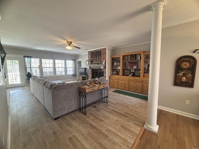 living room with a brick fireplace, ornamental molding, decorative columns, wood finished floors, and a ceiling fan