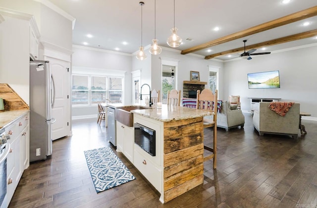 kitchen with a sink, dark wood finished floors, appliances with stainless steel finishes, a breakfast bar area, and a stone fireplace