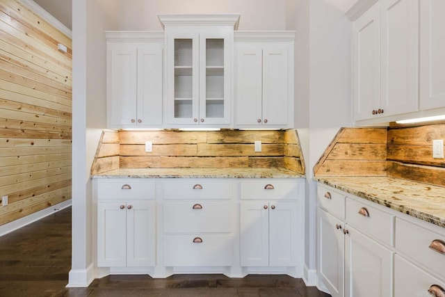 kitchen featuring light stone counters, wooden walls, white cabinetry, and glass insert cabinets