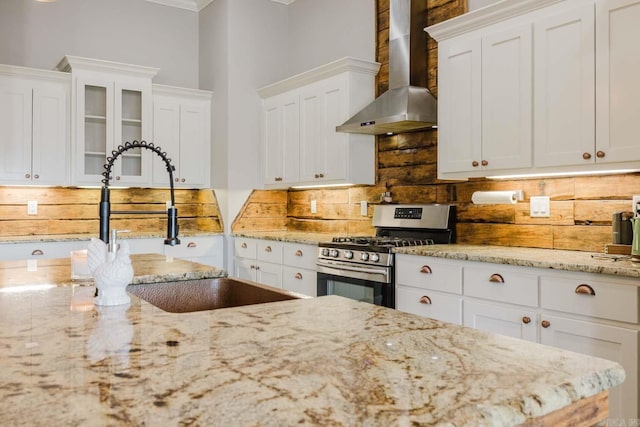 kitchen featuring stainless steel range with gas stovetop, white cabinets, wall chimney exhaust hood, and decorative backsplash