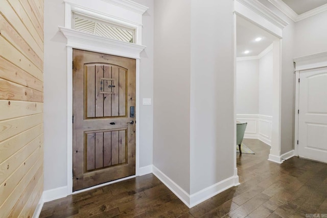 foyer entrance featuring a decorative wall, baseboards, crown molding, and dark wood-type flooring