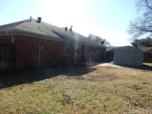 back of property with an outdoor structure, a lawn, brick siding, and a shed