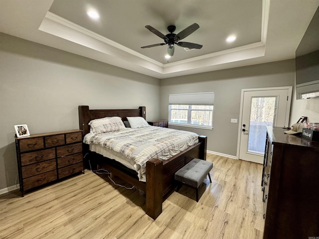 bedroom with a tray ceiling, light wood-style flooring, and baseboards