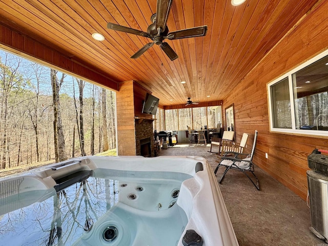 view of patio featuring a ceiling fan, exterior fireplace, and a hot tub