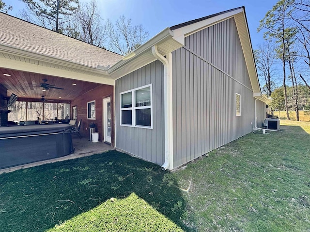 view of property exterior featuring a lawn, a ceiling fan, cooling unit, roof with shingles, and a hot tub