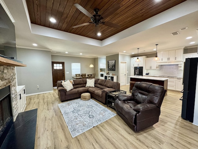 living area with visible vents, light wood-style flooring, a stone fireplace, a raised ceiling, and wooden ceiling