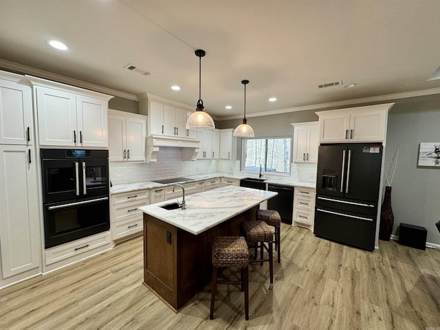 kitchen featuring visible vents, black appliances, a center island with sink, white cabinetry, and light wood-style floors