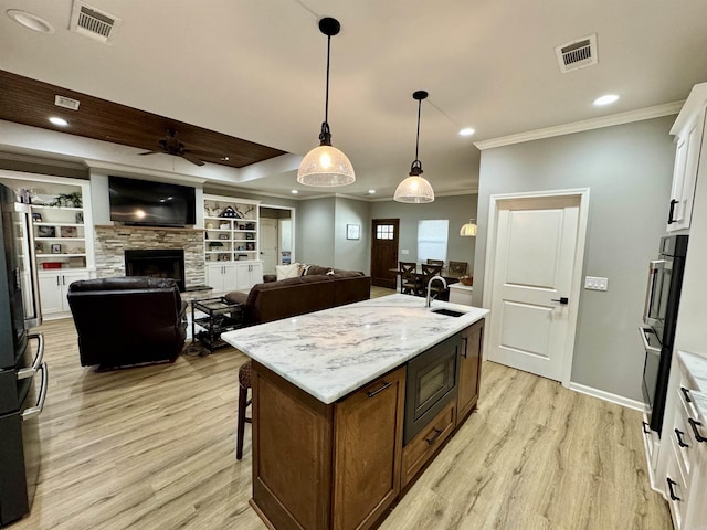 kitchen featuring light wood finished floors, a center island with sink, white cabinets, black appliances, and a sink