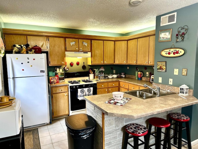 kitchen featuring visible vents, range with gas cooktop, under cabinet range hood, freestanding refrigerator, and a sink