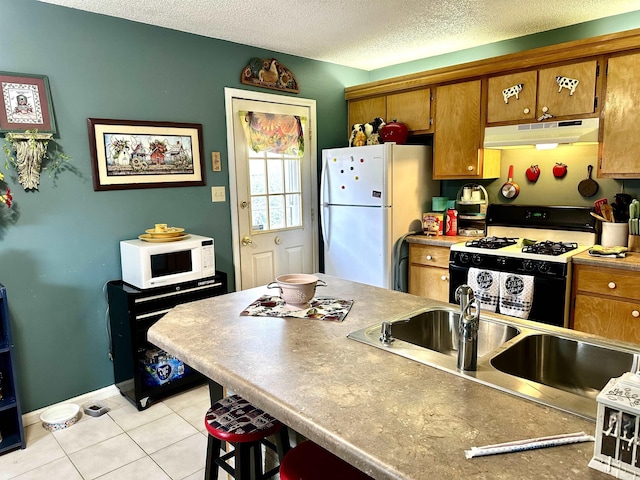 kitchen featuring under cabinet range hood, brown cabinets, white appliances, a textured ceiling, and a sink