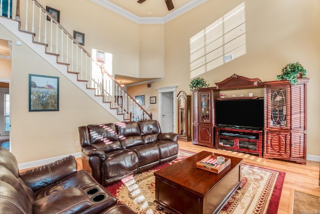 living room with crown molding, baseboards, stairway, light wood-style floors, and a towering ceiling