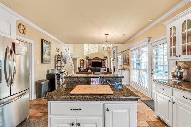 kitchen featuring stone tile flooring, glass insert cabinets, crown molding, and stainless steel refrigerator with ice dispenser