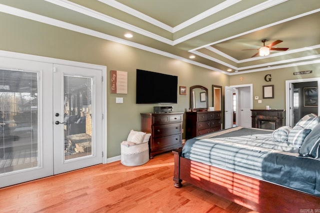 bedroom with access to exterior, light wood finished floors, a tray ceiling, ornamental molding, and french doors