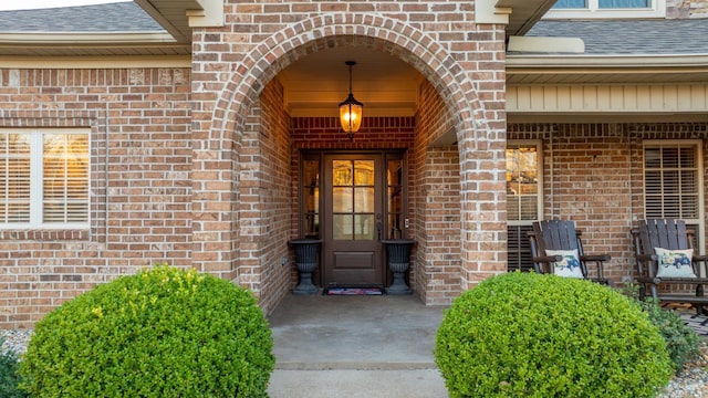 entrance to property featuring brick siding and a shingled roof