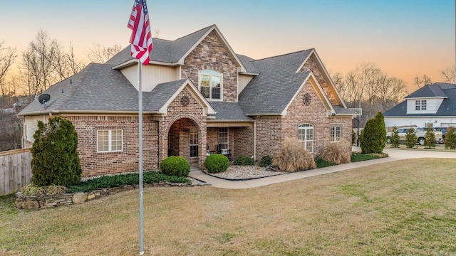 view of front of property featuring stone siding, brick siding, roof with shingles, and a front yard