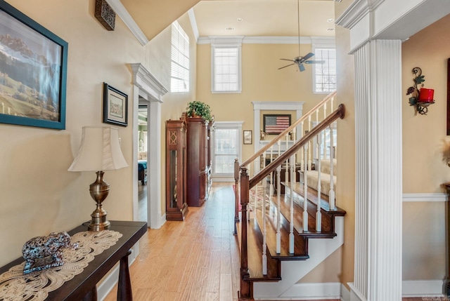 stairway with crown molding, baseboards, a towering ceiling, wood finished floors, and a ceiling fan