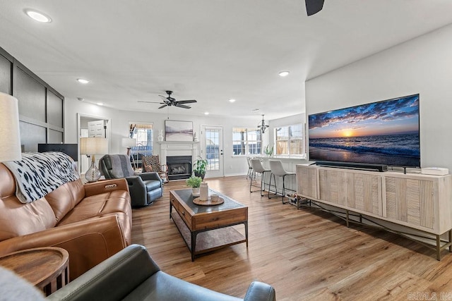 living area featuring a fireplace, plenty of natural light, a ceiling fan, and light wood finished floors