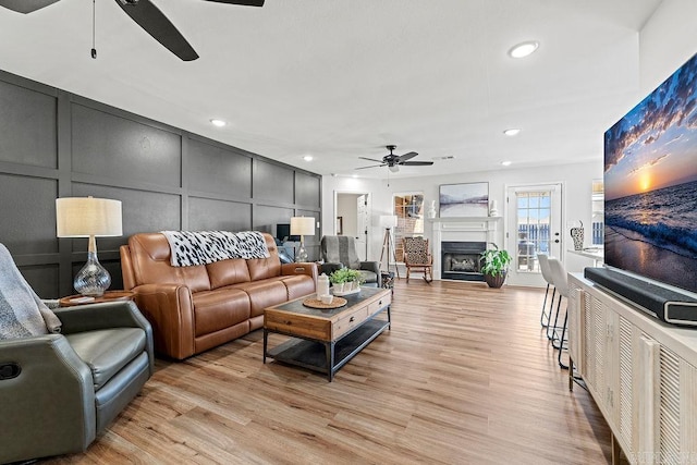 living area with light wood finished floors, recessed lighting, a fireplace, ceiling fan, and a decorative wall