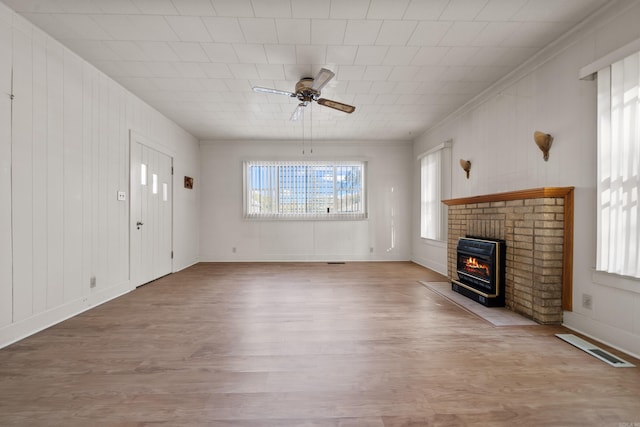 unfurnished living room featuring a ceiling fan, visible vents, light wood-style flooring, crown molding, and a brick fireplace