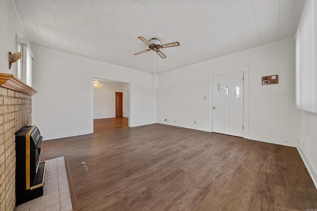 unfurnished living room with baseboards, a wood stove, a ceiling fan, and wood finished floors