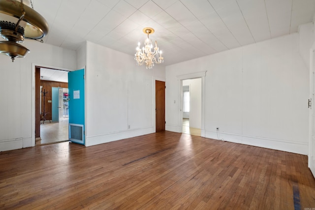 unfurnished room with hardwood / wood-style floors, a notable chandelier, and visible vents