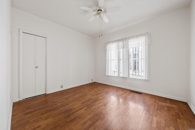 unfurnished bedroom featuring visible vents, ceiling fan, baseboards, hardwood / wood-style floors, and a closet