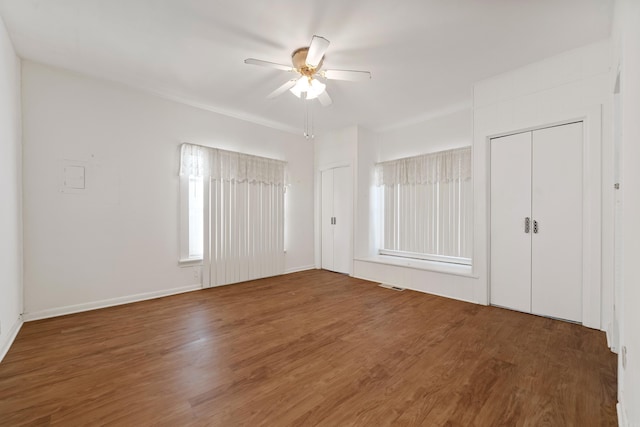 unfurnished bedroom with visible vents, a ceiling fan, multiple closets, and wood finished floors