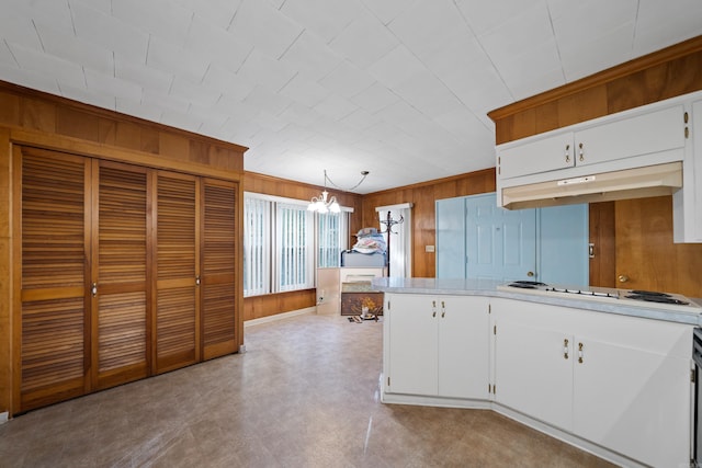 kitchen featuring under cabinet range hood, white cabinetry, wooden walls, and light countertops