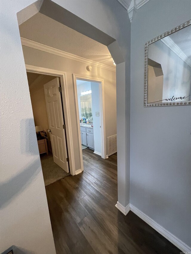 hall featuring dark wood finished floors, visible vents, crown molding, and baseboards