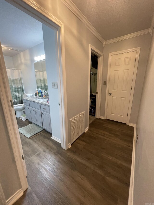 corridor with visible vents, crown molding, baseboards, a textured ceiling, and dark wood-style flooring