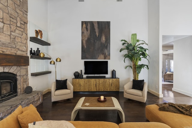 living area with a fireplace, baseboards, a towering ceiling, and wood finished floors