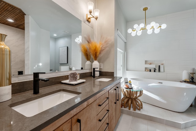 full bathroom with double vanity, a freestanding bath, a sink, tile walls, and a notable chandelier