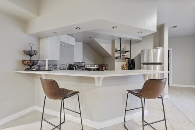 kitchen featuring tasteful backsplash, white cabinetry, appliances with stainless steel finishes, a breakfast bar area, and a peninsula